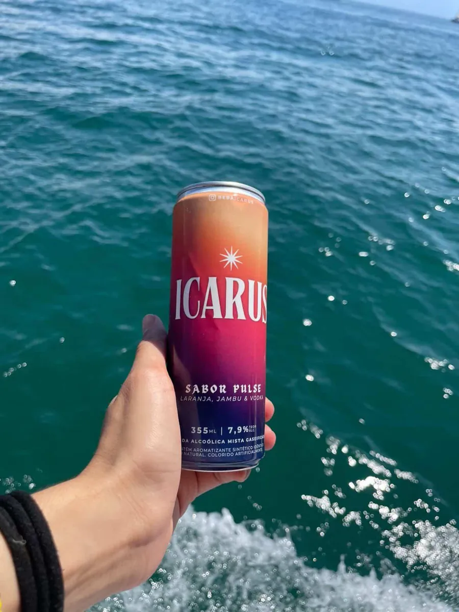 Mão segurando uma lata de ICARUS sobre o mar